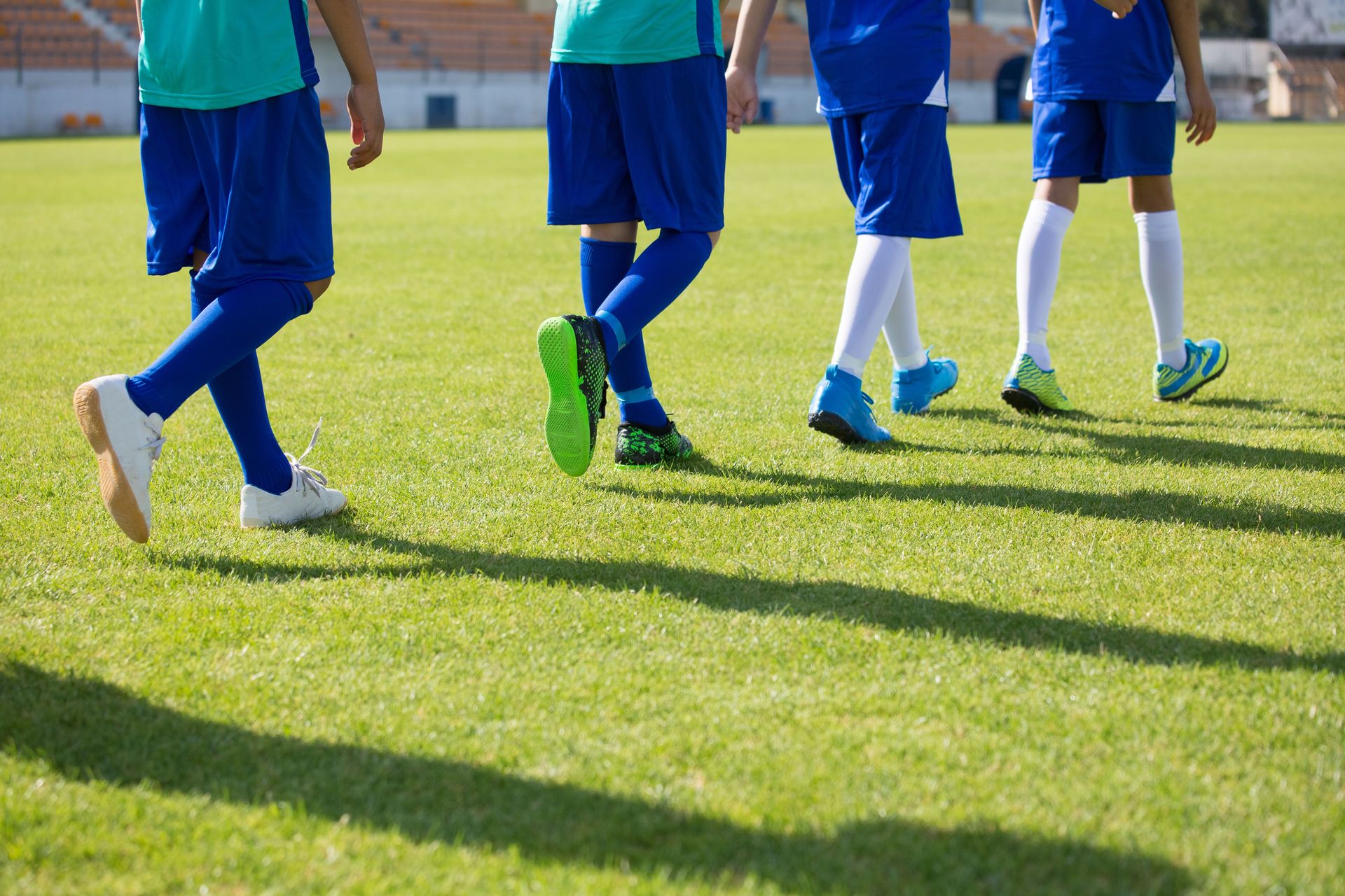 Group of children wearing blue sports uniforms walking on a sunny football field.